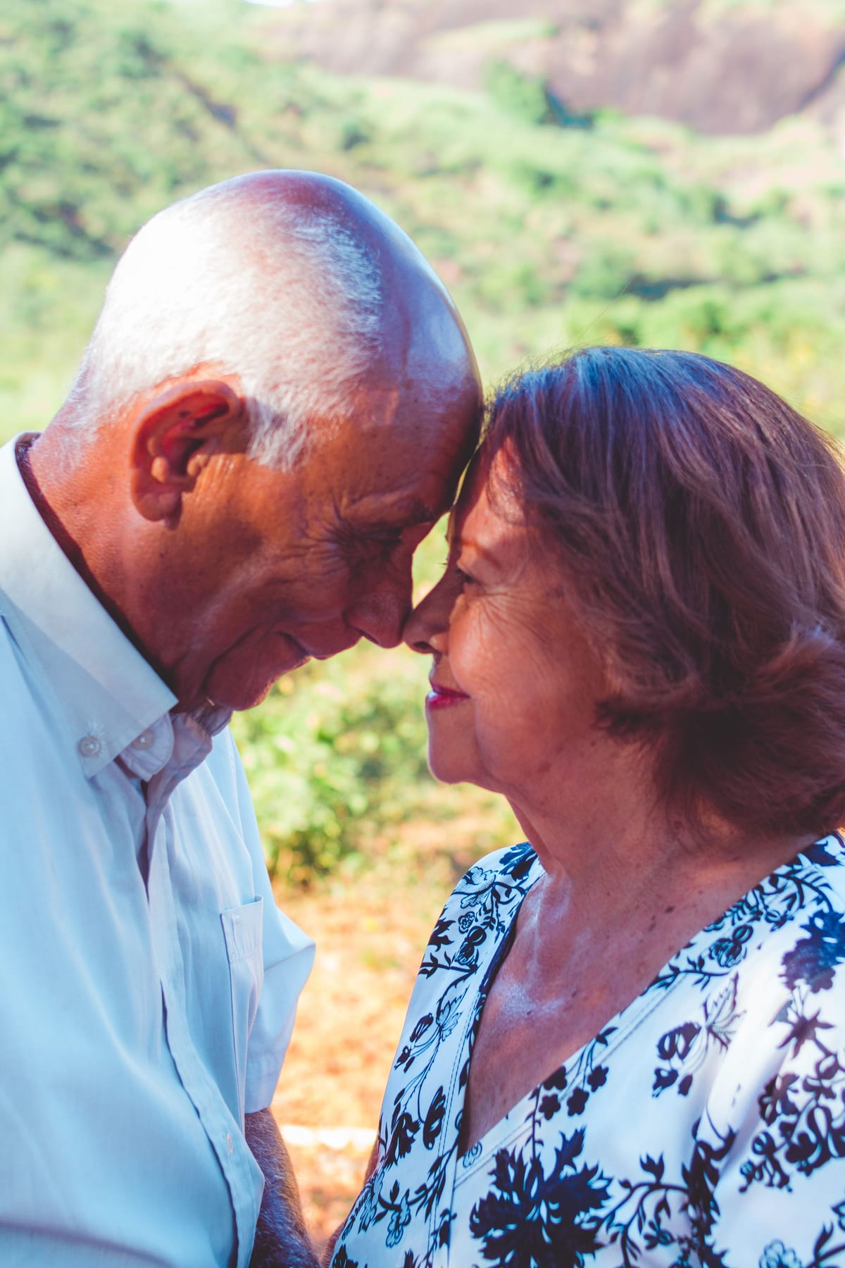 Casal idoso com as testas encostadas, ao ar livre
